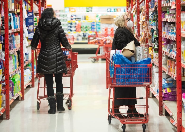 Dos mujeres con carritos de compras caminan por el pasillo de una tienda de comestibles.