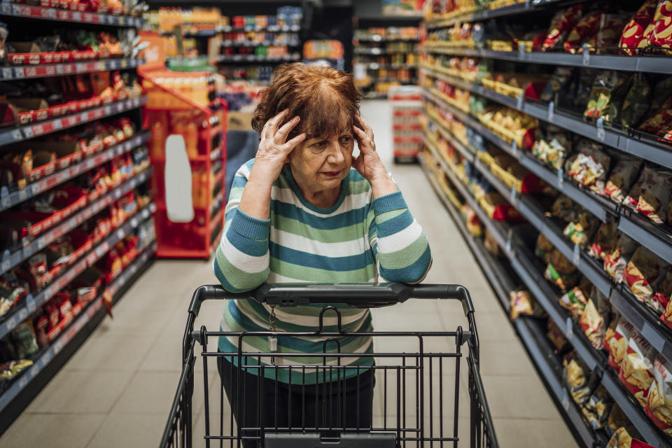 Mujer mayor parada en el pasillo de productos del supermercado y preocupada por el aumento de los precios de los comestibles