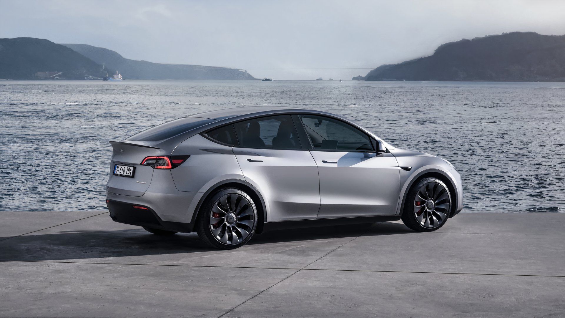 Gray Tesla Model Y. está estacionado por el agua. 