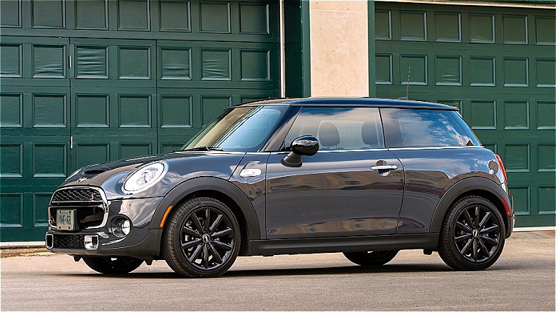 Un mini coopper gris estacionado en la calle frente a las puertas de garaje verde.