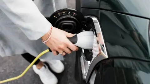 Getty Images La foto muestra la mano de una mujer conectando un cargador eléctrico a un coche negro.