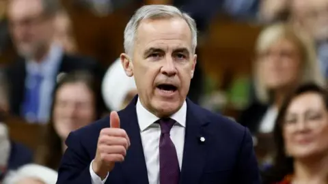 Reuters El primer ministro canadiense, Mark Carney, habla durante el período de preguntas en la Cámara de los Comunes en la Colina del Parlamento en Ottawa, Ontario, Canadá. Viste un traje azul oscuro y una corbata de color morado oscuro, y levanta el pulgar a mitad de su discurso mientras se dirige a la Cámara de Representantes. 