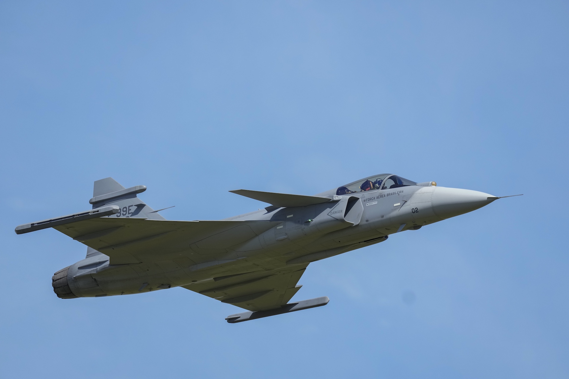 Un avión de combate gris en vuelo contra un cielo azul sin nubes.